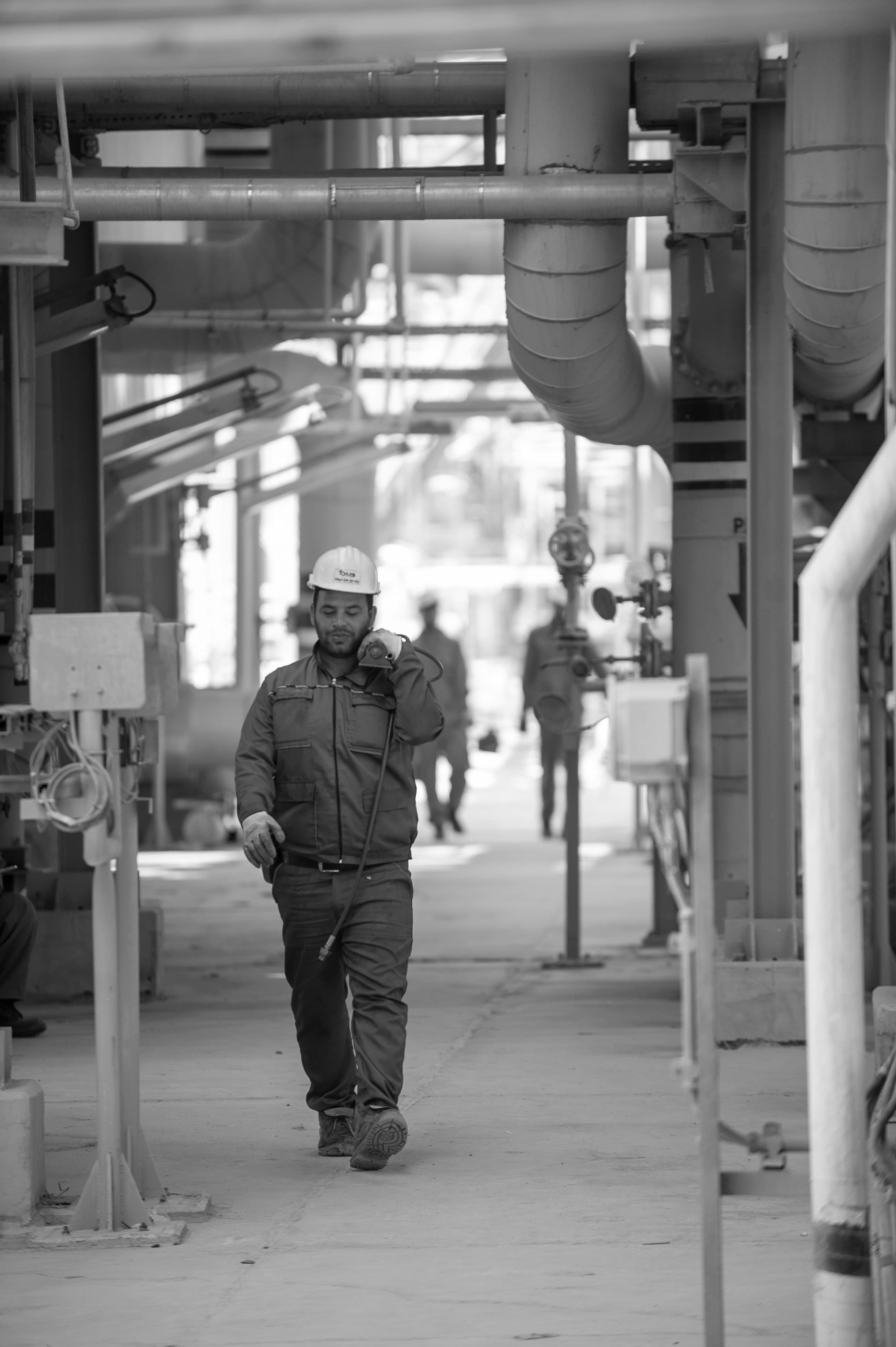 Technicus met helm loopt zelfverzekerd door een procesinstallatie